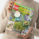 Person im beigefarbenen Strickpullover hält eine schräg ausgerichtete Gartenzeitschrift mit grünem Rand und farbiger Titelgestaltung. Sichtbare Texte: „Praxis-Tipps für Balkon und Garten“, „Blumen & Pflanzen“, „September 2026“, „Herbst-Anemonen – die schönsten Sorten“, „Neue Pflanz-Ideen: Blütenreicher Spätsommer“ sowie Hinweise zu Tischdeko, DIY-Projekten, Herbstsalaten, Balkon und Terrasse und Ziergräsern.