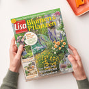Schräg liegendes Magazin „Lisa Blumen & Pflanzen“ aus glänzend bedrucktem Papier, von zwei Händen mit grün-grauen Ärmeln gehalten. Das Cover zeigt einen blühenden Garten mit gelben, rosa, weißen und violetten Blumen sowie Balkon- und Terrassenbildern; lesbare Texte: „Praxis-Tipps für Balkon und Garten“, „Blumen & Pflanzen“, „Blumen & Pflanzen“, „Jetzt freuen wir uns auf:“, „Neue Pflanz-Ideen: Blütenreicher Spätsommer“ und „Herbst-Anemonen – die schönsten Sorten“.