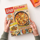 Aufgeschlagene Zeitschrift „Lisa kochen & backen“ auf weißem Tisch, von zwei Händen ohne erkennbare Geschlechtsmerkmale gehalten. Das Cover zeigt einen schwarzen Topf mit cremigem Gericht, Hackbällchen, Kartoffeln und Gemüse sowie Texte wie „Einfache Rezepte, die alle begeistern“, „One Pot Süßkartoffel-Topf mit Hackbällchen“, „Lauter Goldstücke“ und „30-Minuten-Hits“; oben rechts liegt ein orangefarbenes Küchenutensil.