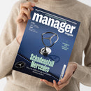 Eine Person im beigefarbenen Strickpullover hält ein dunkelblaues Magazin mit dem Titel „manager magazin“ und der Datumsangabe „AUGUST 2026“ in beiden Händen. Auf dem Cover stehen unter anderem „KI-DUELL: Wie Anthropic OpenAI überholt“, „QIAGEN: Der Biotech-Pionier stürzt ab“, „KLAUS-MICHAEL KÜHNE: Ein Patriarch im Kaufrausch“ und „Schadensfall Mercedes: Wie Ola Källenius die Edelmarke abwirtschaftet“; mittig sind ein Mercedes-Stern und eine silberne Kühlerfigur abgebildet.