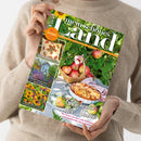 Person im beigefarbenen Strickpullover hält ein schräg ausgerichtetes Magazin aus bedrucktem Papier in beiden Händen. Auf dem grünen Cover stehen „mein schönes Land“, „Gutes bewahren · Schönes entdecken · September“, „Geschenke der Natur“ und „30 Seiten kreativ durch den Herbst“; abgebildet sind Sonnenblumen, Äpfel, ein Korb, Apfelkuchen, ein Garten und Blüten.