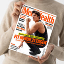 Schräg gehaltene Zeitschrift „Men’s Health“ mit weißem Cover, orange-schwarzer Typografie und männlicher Person im schwarzen Sportshirt beim Hocken und Anspannen des Arms. Lesbare Texte: „Selbst-Check: Bin ich schon wie mein Vater?“, „Longevity-Food“, „Nicholas Galitzine“, „Das stärkt dein Herz“, „Deine neue Blitz-Challenge: FIT IN NUR 21 TAGEN“ sowie „PLUS: Padel-Tennis, Protein-Shakes, Jacken-Trends“.