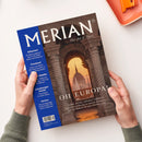Zwei Hände halten schräg eine MERIAN-Reisezeitschrift mit dem Titel „MERIAN“ und dem Untertitel „The Art of Travel“. Das Cover zeigt einen steinernen Torbogen mit Blick auf das Budapester Parlamentsgebäude bei Sonnenuntergang; blaue Seitenleiste mit „Albanien“, „Finnland“, „Die schönsten Städte“, „Lüneburger Heide“ und „Istrien“ sowie der Überschrift „OH EUROPA!“.