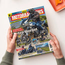 Schräg auf einer weißen Fläche liegende Motorradzeitschrift „MOTORRAD NEWS“, von zwei Händen gehalten. Das Titelbild zeigt eine helmtragende Person in dunkler Motorradkleidung auf einem silbernen Motorrad mit „HONDA“-Schriftzug; lesbare Texte sind „SERVICE: MOTORRAD UND HITZE“, „Schon gefahren! KTM 790 Duke, Norton Atlas“, „FAHRBERICHT: HONDA CB 1000 F Retro-Hornet“ und „REISEBILDER Schottland & Türkei“.