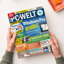 Schräg gehaltenes Titelblatt der Zeitschrift „PC WELT“ mit blauem Design, weißen und gelben Überschriften „Windows Pro gratis!“, „2 Doppel-DVDs + 32 Seiten Extra“, „Update mit 1-Klick“ und „WLAN-Tuning“. Zwei nicht näher bestimmbare Hände in grauen Strickärmeln halten das Magazin; oben rechts liegt ein orangefarbener Gegenstand auf weißer Fläche.