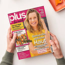 Aufgeschlagenes Magazin „plus für mich“ mit pink-gelbem Cover, gehalten von zwei Händen. Das Titelbild zeigt eine blonde Frau in gelbem Oberteil; sichtbare Texte: „Gesunde, schöne Haut“, „Glanz ins Haar“, „Das beruhigt den Magen“, „Luxus-Camping in Dänemark“, „Saisonal & regional“ und „Einmal im Leben …“. Daneben liegt oben rechts ein orangefarbenes Objekt.