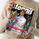 Eine Person im beigefarbenen Strickpullover hält ein schräg fotografiertes Magazin mit schwarzem Cover. Darauf sind der Tennisspieler Jannik Sinner in weißem Tennisoutfit mit goldenem Pokal sowie die Texte „tennis MAGAZIN“, „SEIT 50 JAHREN DIE NR. 1“, „GOLDJUNGE“, „Sinner schlägt Zverev im Wimbledon-Finale“, „GROSSE PLÄNE“, „AUFSTEIGER“ und „STRUFFS LAUF“ erkennbar.