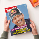 Aufgeschlagenes Magazin mit blauem Cover, gehalten von zwei Händen mit grauen Strickbündchen. Darauf das Gesicht einer männlichen Person mit schwarzer Red-Bull-Kappe sowie die Überschrift „Lars Klingbeil: Macht er so die SPD wieder fit?“, auf weißer Fläche neben einem teilweise sichtbaren orangefarbenen Gegenstand.