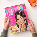 Schräg von oben fotografiertes „TOPModel FRIENDS Club“-Magazin mit pinkem Cover, einer illustrierten dunkelhaarigen Figur mit großer lila Schleife sowie Händen an beiden Seiten. Sichtbare Texte: „Medienzeit“, „Beste-Freundinnen-Sommer“, „Neu im Club?“, „Deine EXTRAS“, „Über 150 Sticker“, „Postkarten“, „2 Poster“, „Malen“, „Gewinnen“ und „Tierisches Wissen“; oben rechts liegt ein orangefarbenes Etui.