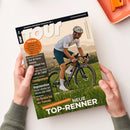 Schräg fotografiertes Fahrradmagazin aus Papier, von zwei Händen vor weißem Hintergrund gehalten. Das Cover zeigt eine männliche Person mit Helm und Sonnenbrille auf einem schwarzen Rennrad in grüner Landschaft; sichtbar sind die Texte „TOUR“, „EUROPAS RENNRAD-MAGAZIN“, „www.tour-magazin.de“, „Räder im Test“, „Tour de France Femmes“, „Deutschland-Tour“, „Standpumpen“, „Regeneration“ und „TOP-RENNER“.