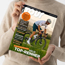 Aufgeschlagenes Rennradmagazin „TOUR“, schräg von oben von einer weiblichen Person im beigefarbenen Strickpullover gehalten. Das Cover zeigt einen männlichen Radfahrer mit weißem Helm auf schwarzem Rennrad sowie die Texte „Europas Rennrad-Magazin“, „www.tour-magazin.de“, „Tour de France Femmes“, „Deutschland-Tour“, „Standpumpen“, „Regeneration“ und „TOP-NEUE RENNER“.