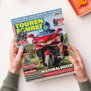 Diagonal gehaltenes Magazin „TOURENFAHRER“ mit dem Titel „REISERETTUNG: ERSTE HILFE BEI NOTFÄLLEN“ und dem Hauptthema „MAXIMALBOXER“, darunter eine rote Tourenmaschine mit Helm tragender Person. Weitere sichtbare Texte: „Reportagen • Test • Technik“, „Touren-Test BMW F 450 GS Trophy“, „Test Reisestiefel – Halbhoch und dicht“, „Große Gefühle Royal Enfield Classic 650“ und „AufTanken: Rheintäler, Ardèche, Kasachstan“; zwei Hände halten das Magazin vor weißem Hintergrund.