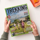 Schräg fotografierte Zeitschrift „TREKKING“ mit grünem Rand und Titel „WANDERN & OUTDOOR“, in zwei Händen über weißer Fläche gehalten. Das Cover zeigt drei wandernde Personen vor alpiner Landschaft und sichtbare Texte wie „14 Traumwege“, „Trentino“, „Irlands Südwesten“, „Tour der Kontraste“, „Sommerbekleidung“ sowie „Ratgeber Energiemanagement“.