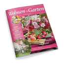 Schräg fotografierte, glänzende Zeitschrift „Wohnen & Garten“ mit pinkfarbenem Cover und dem Text „Die schönsten Ideen für drinnen und draußen“, „September 2026“ sowie „Blüten-Finale in Rosé“. Abgebildet sind ein Blumenstrauß im grünen Topf, Äpfel und Beeren auf einem Tisch, eine Suppenschüssel, ein Haus mit Garten und eine nicht näher erkennbare Person; weitere Texte nennen „Garten & Pflanzen“, „Ländliches Spätsommerglück in Schweden“, „Wohnen“, „Garten“ und „Dekorieren“.