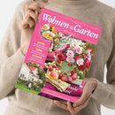 Weibliche Person im beigen Strickpullover hält ein schräg fotografiertes, pinkes Magazin „Wohnen & Garten“ mit dem Titel „Die schönsten Ideen für drinnen und draußen“ und „September 2026“. Das Cover zeigt Blumenarrangements, Äpfel, ein Haus sowie die Texte „Stilvoll einrichten mit edlen Paisley-Mustern“, „Diese Dahlien-Sorten lassen Beete leuchten“ und „Terrassen kreativ in Purpurtönen gestalten“.