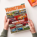 Schräg von oben fotografierte Zeitschrift „YOUNGTIMER“ auf weißer Fläche, von zwei Händen gehalten, mit orangefarbener Ablage und Klammer rechts oben. Das Cover zeigt mehrere klassische Fahrzeuge und die Texte „MotorKlassik“, „DIE KULT-KLASSIKER DER 70ER, 80ER UND 90ER“, „JULI/AUGUST 2026“ sowie „HIGH FIVE! Warum Fünfzylinder besonders viel Spaß machen“.